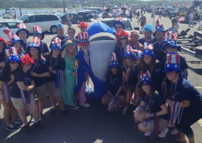 group photo of Moby Dick's restaurant staff dressed in Patriotic attire with person dressed in whale costume in front of the harbor