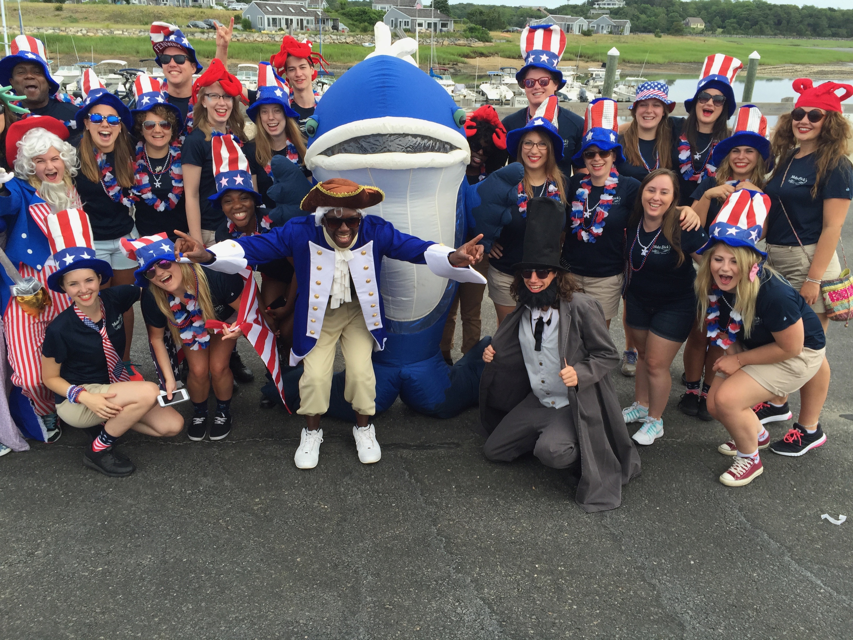 group photo of Moby Dick's restaurant staff dressed in Patriotic attire with person dressed in whale costume in front of the harbor